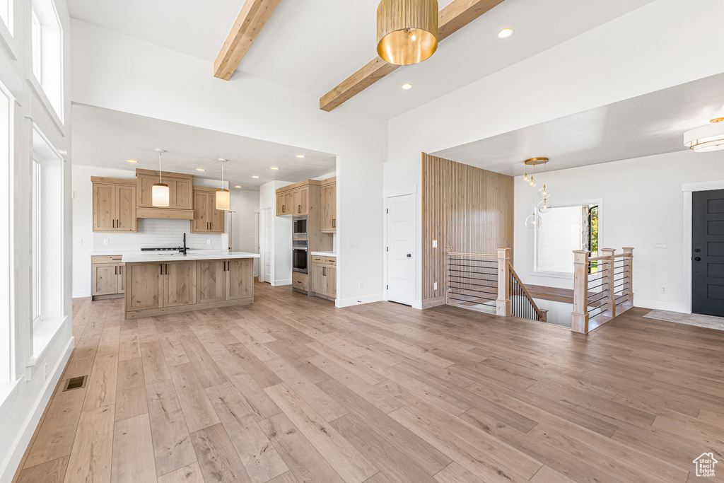 Unfurnished living room featuring a high ceiling, light hardwood / wood-style floors, sink, and beamed ceiling