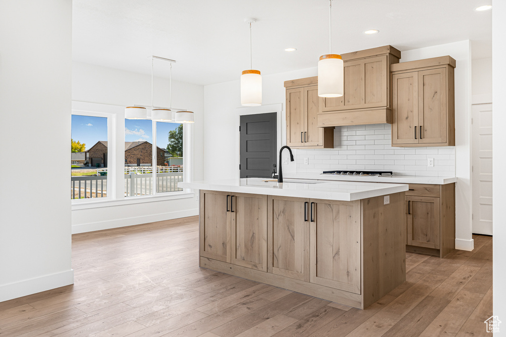 Kitchen featuring tasteful backsplash, sink, an island with sink, hanging light fixtures, and light hardwood / wood-style flooring