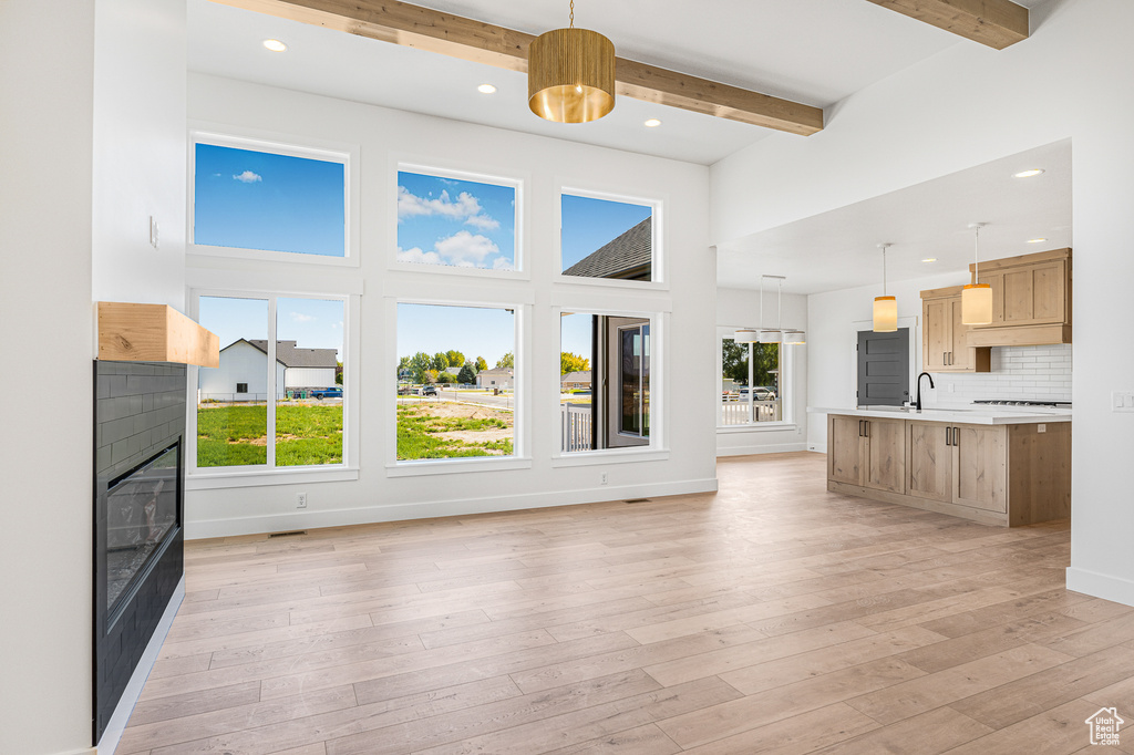 Unfurnished living room featuring light hardwood / wood-style flooring, sink, beamed ceiling, and plenty of natural light