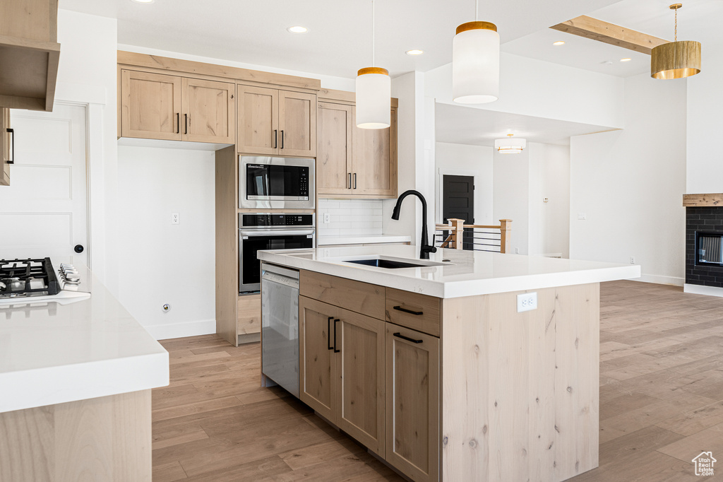 Kitchen with light brown cabinetry, pendant lighting, appliances with stainless steel finishes, and light hardwood / wood-style floors