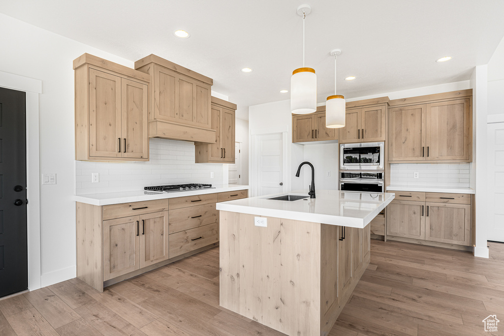 Kitchen with appliances with stainless steel finishes, hanging light fixtures, light hardwood / wood-style floors, decorative backsplash, and sink