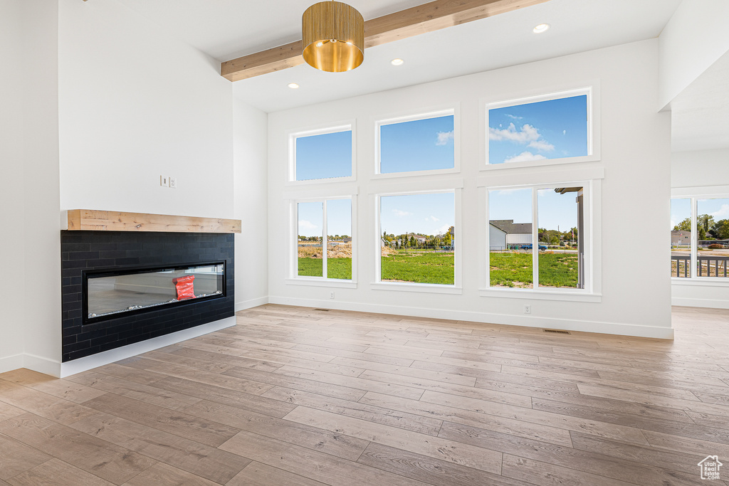 Unfurnished living room featuring light hardwood / wood-style flooring, beam ceiling, and a healthy amount of sunlight