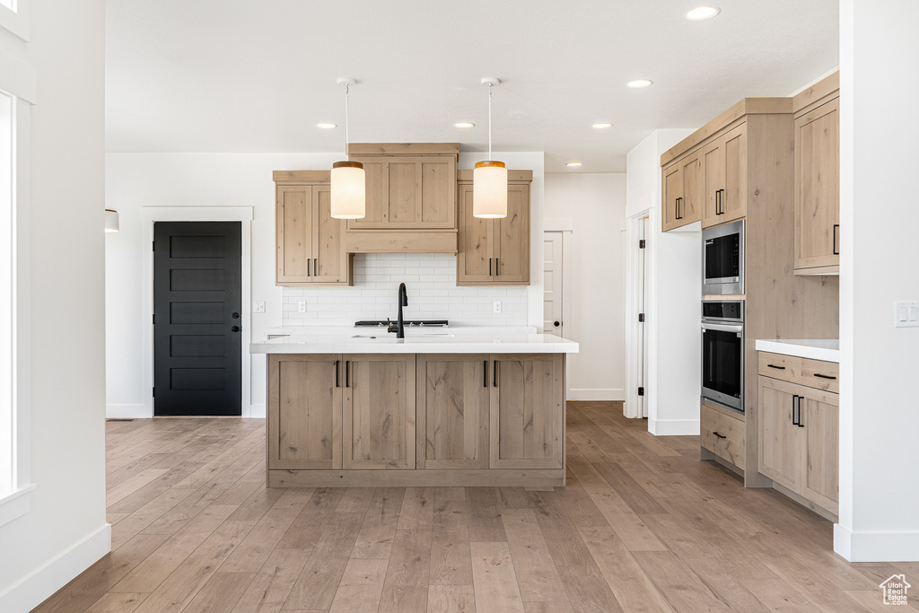 Kitchen featuring light brown cabinetry, stainless steel appliances, hanging light fixtures, and light hardwood / wood-style flooring