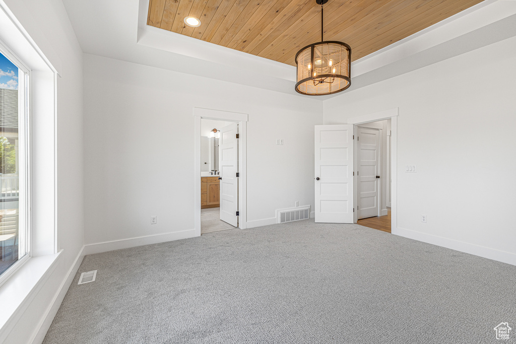 Carpeted spare room with a raised ceiling, wood ceiling, an inviting chandelier, and a wealth of natural light