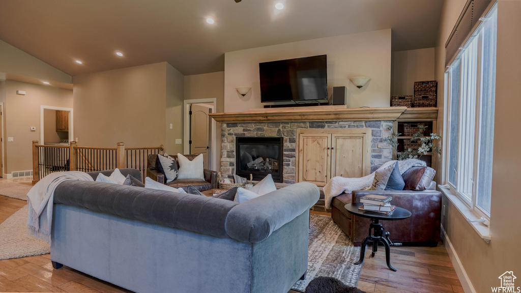 Living room featuring light wood-type flooring, a wealth of natural light, a stone fireplace, and vaulted ceiling