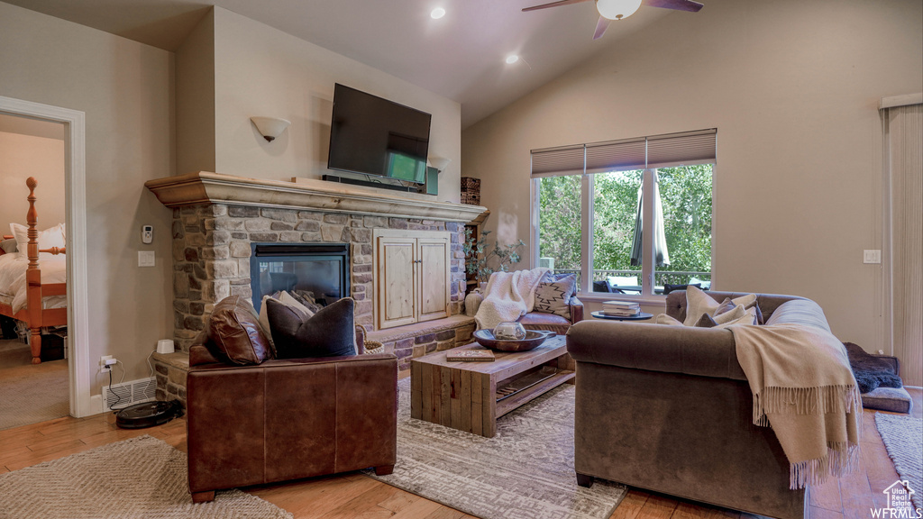 Living room with light hardwood / wood-style flooring, a stone fireplace, ceiling fan, and high vaulted ceiling