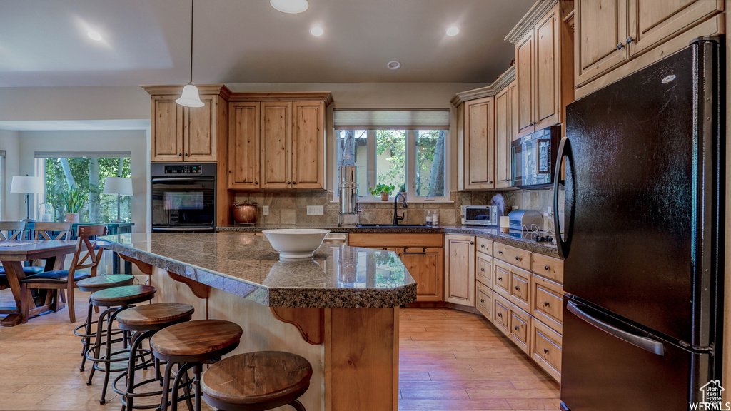 Kitchen featuring decorative backsplash, sink, black appliances, light wood-type flooring, and a kitchen island