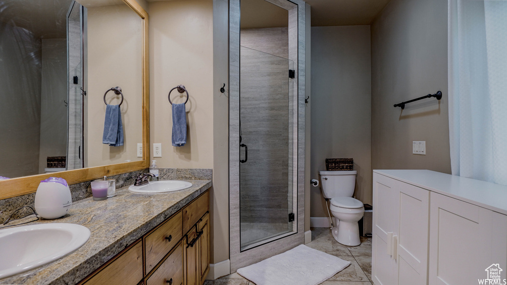 Bathroom featuring dual bowl vanity, a shower with shower door, tile patterned flooring, and toilet