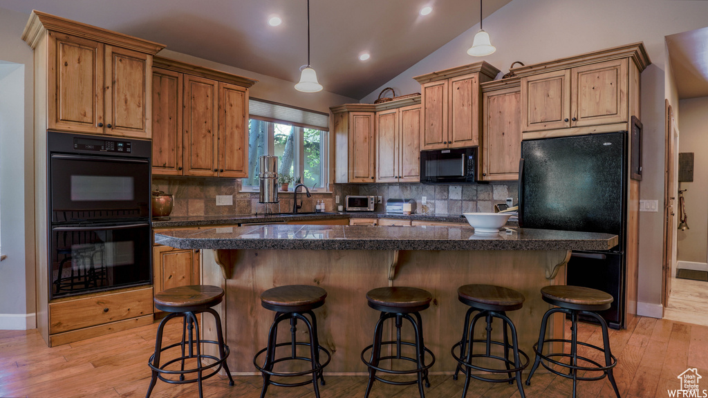 Kitchen with black appliances, pendant lighting, light hardwood / wood-style flooring, and vaulted ceiling