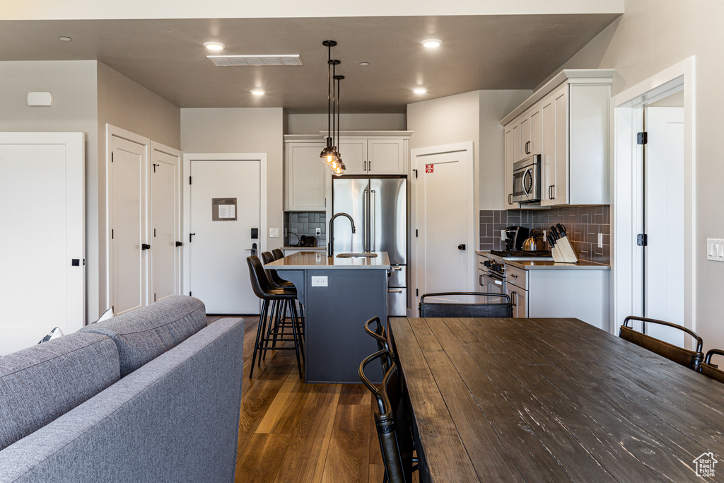 Kitchen with tasteful backsplash, a kitchen breakfast bar, dark hardwood / wood-style flooring, pendant lighting, and a kitchen island with sink