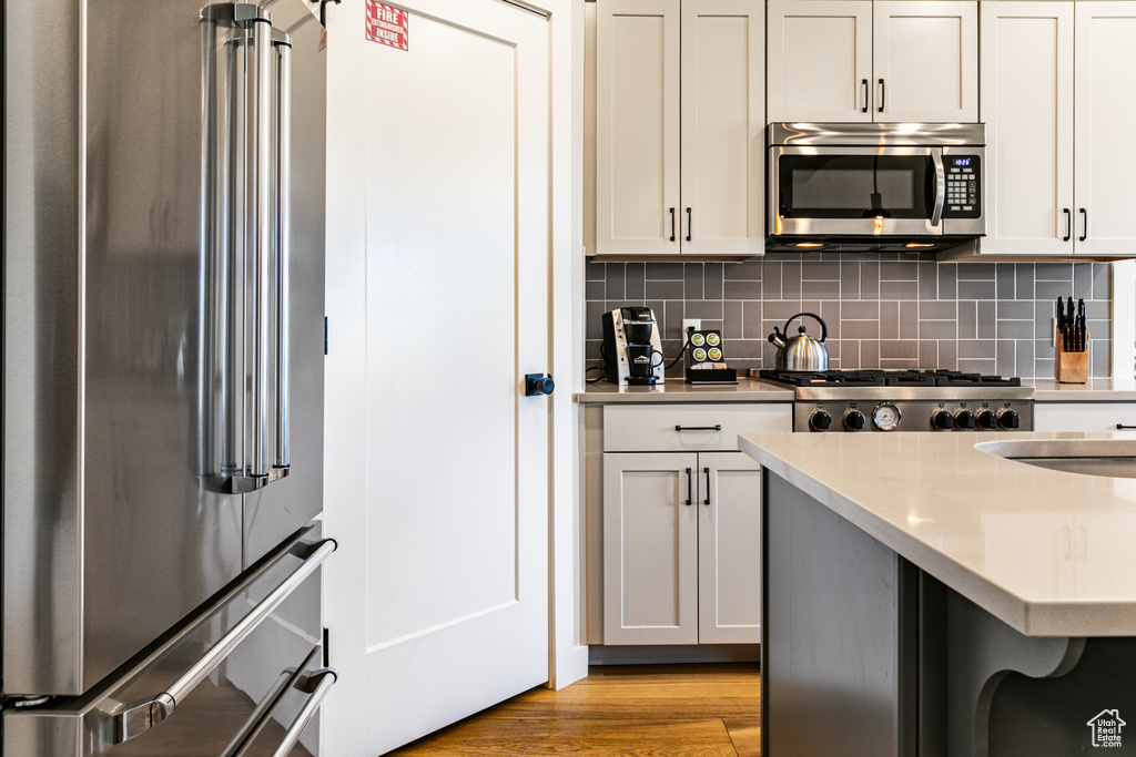 Kitchen with appliances with stainless steel finishes, backsplash, a kitchen bar, and light hardwood / wood-style floors