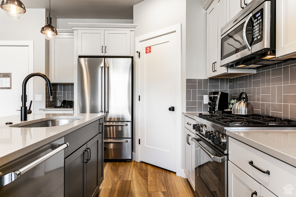 Kitchen featuring high quality appliances, backsplash, hanging light fixtures, and light hardwood / wood-style floors