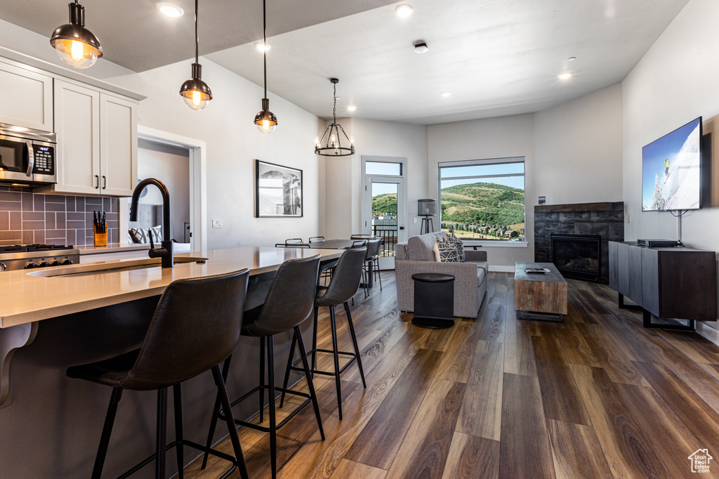 Kitchen with a fireplace, white cabinetry, backsplash, dark hardwood / wood-style floors, and a kitchen bar