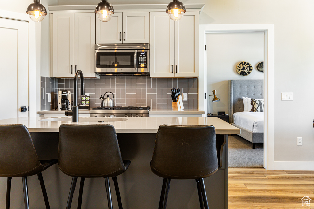 Kitchen featuring a kitchen bar, hanging light fixtures, light hardwood / wood-style floors, and backsplash