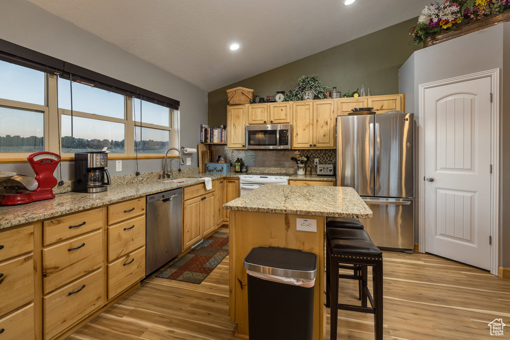 Kitchen featuring vaulted ceiling, light hardwood / wood-style flooring, appliances with stainless steel finishes, and a kitchen island