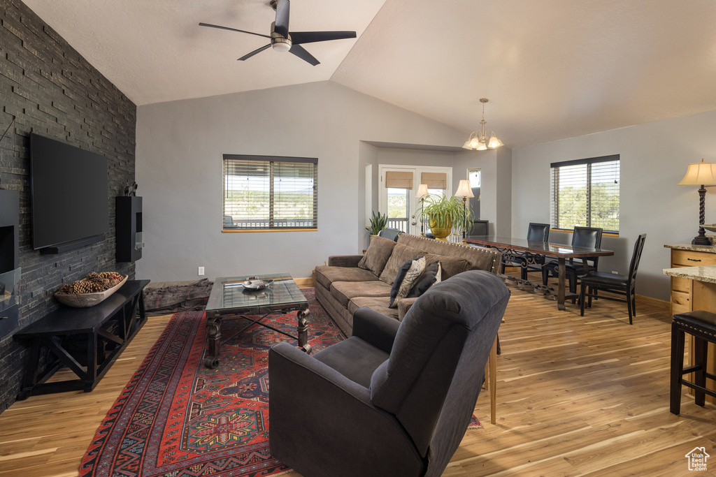 Living room with light hardwood / wood-style flooring, lofted ceiling, and ceiling fan with notable chandelier