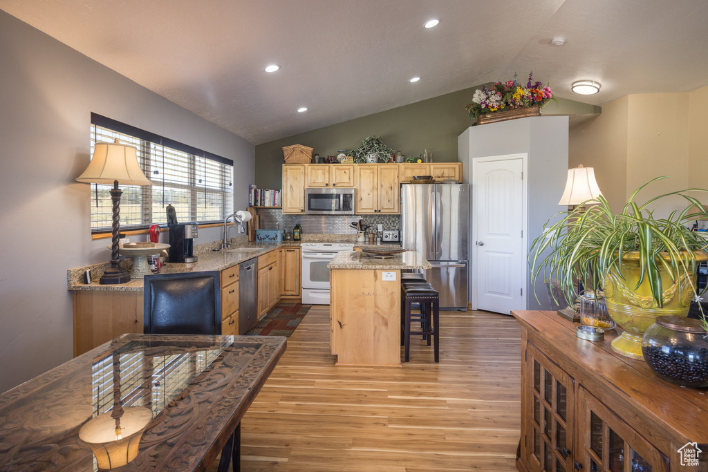 Kitchen featuring appliances with stainless steel finishes, tasteful backsplash, vaulted ceiling, light hardwood / wood-style floors, and light brown cabinetry