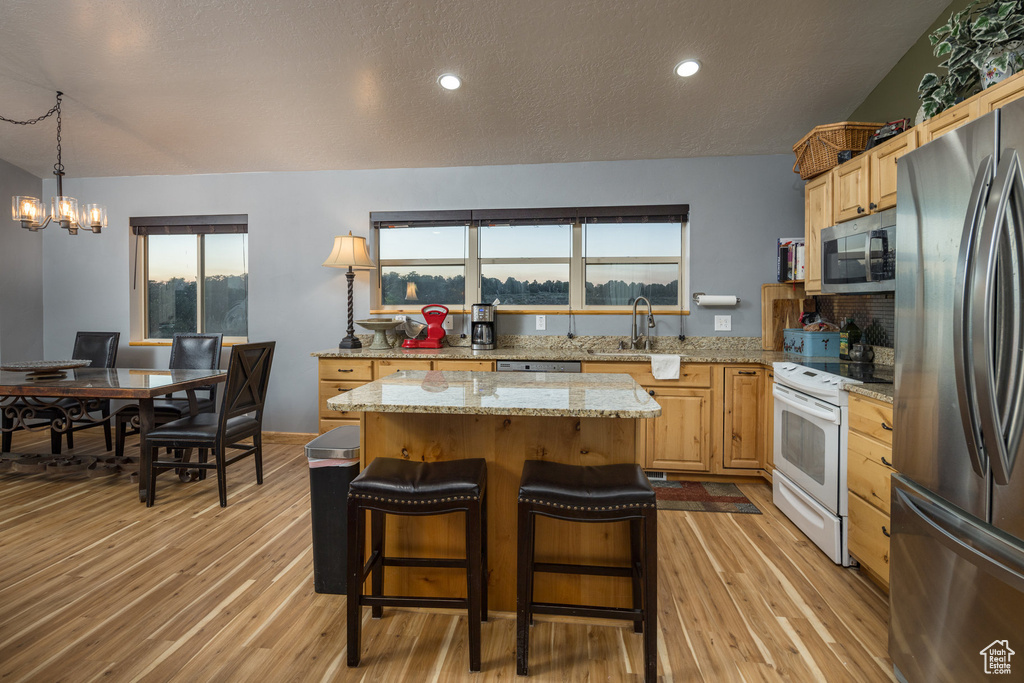 Kitchen with stainless steel appliances, sink, an inviting chandelier, light stone counters, and light hardwood / wood-style floors