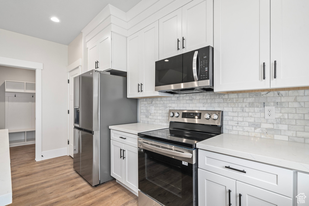 Kitchen with tasteful backsplash, light wood-type flooring, appliances with stainless steel finishes, and white cabinets