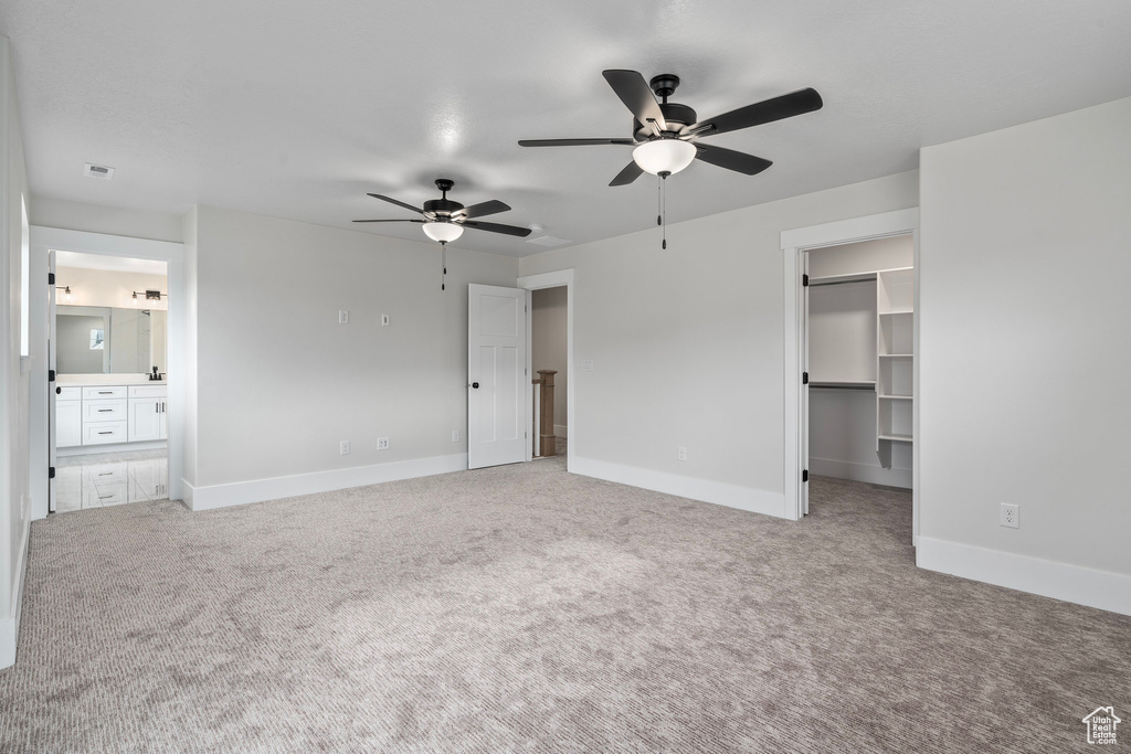 Unfurnished bedroom with connected bathroom, carpet, a spacious closet, a closet, and ceiling fan