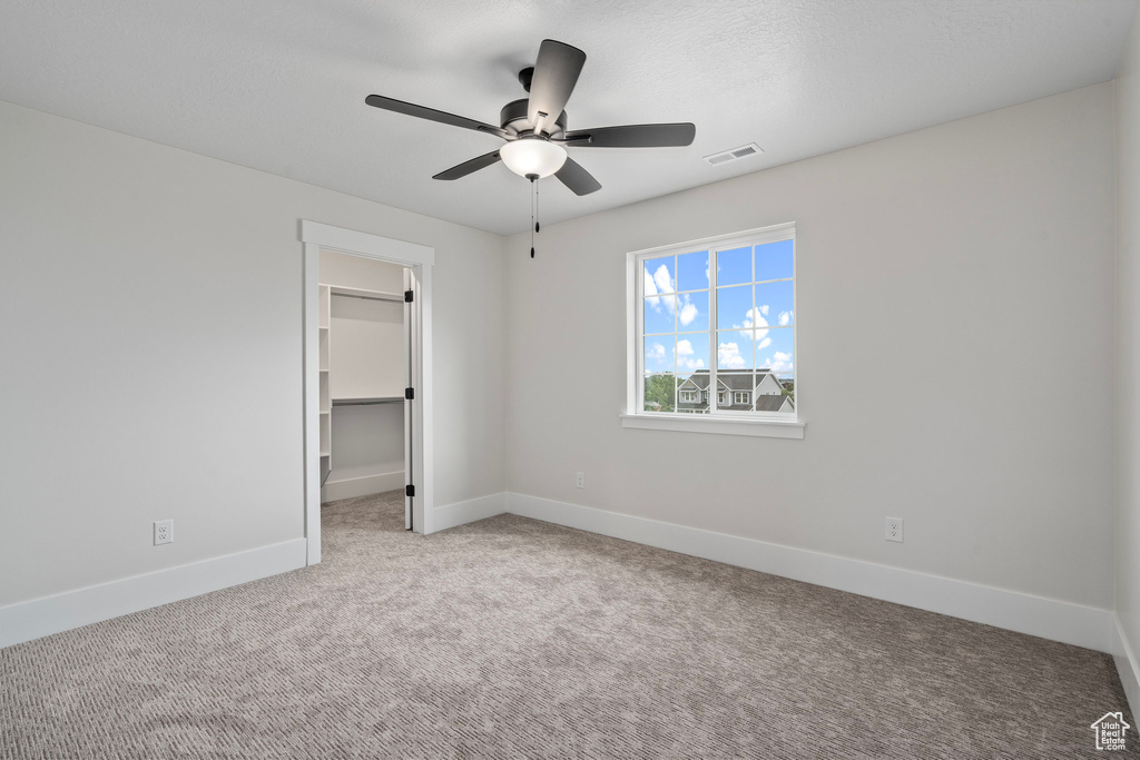 Unfurnished bedroom with ceiling fan, a closet, a spacious closet, and light carpet