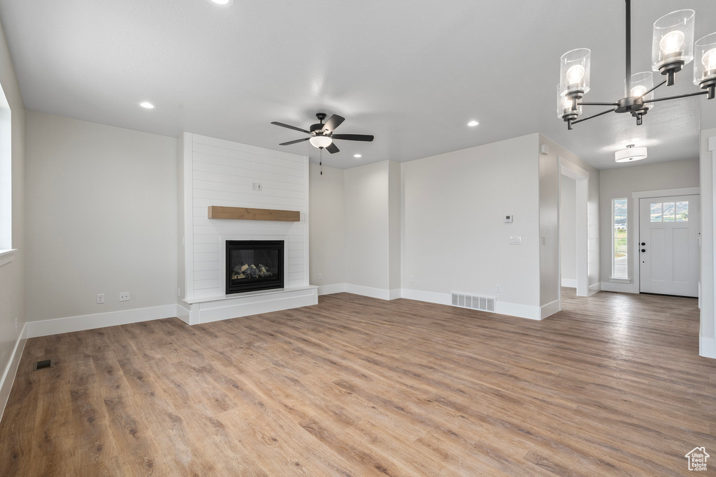 Unfurnished living room featuring a large fireplace, ceiling fan with notable chandelier, and hardwood / wood-style flooring