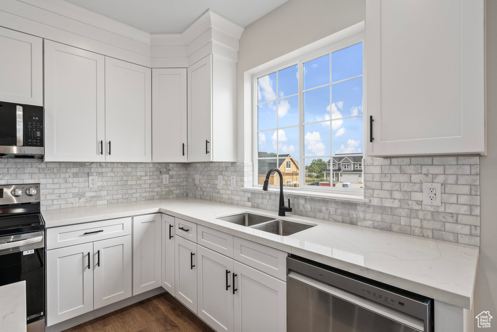 Kitchen with appliances with stainless steel finishes, dark hardwood / wood-style floors, sink, and white cabinetry