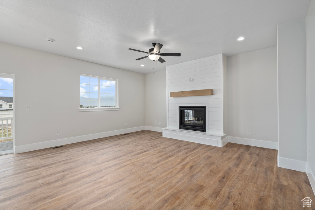 Unfurnished living room with ceiling fan, light wood-type flooring, a fireplace, and wood walls