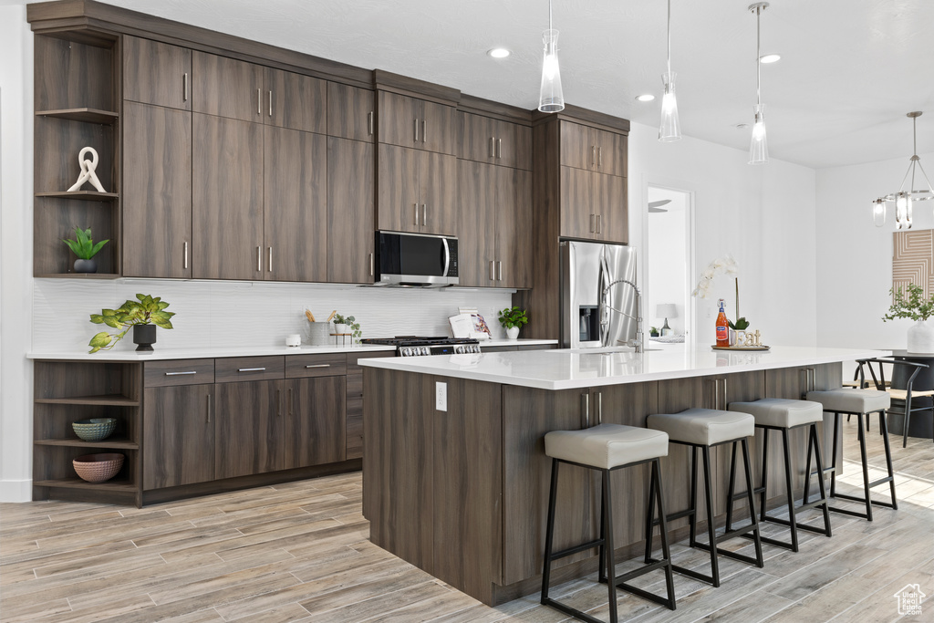 Kitchen featuring open shelves, stainless steel appliances, decorative backsplash, a breakfast bar, and recessed lighting