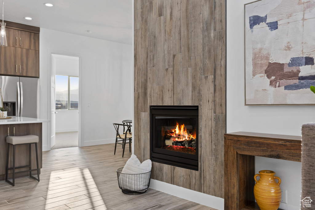 Detailed view of stainless steel refrigerator with ice dispenser, a lit fireplace, wood finished floors, and recessed lighting