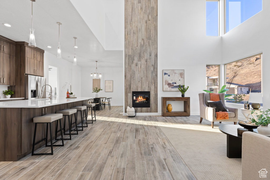Living area featuring a high ceiling, light wood finished floors, a large fireplace, recessed lighting, and a chandelier