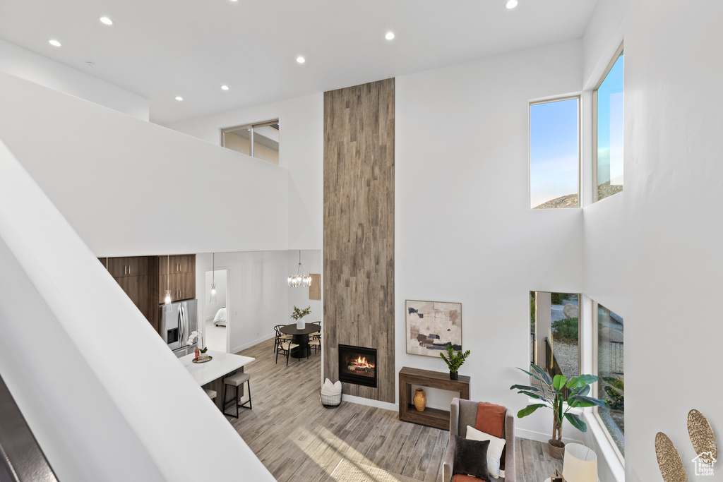 Living area with recessed lighting, light wood finished floors, a chandelier, and a towering ceiling