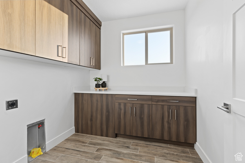 Washroom with hookup for an electric dryer, cabinet space, and light wood-style flooring