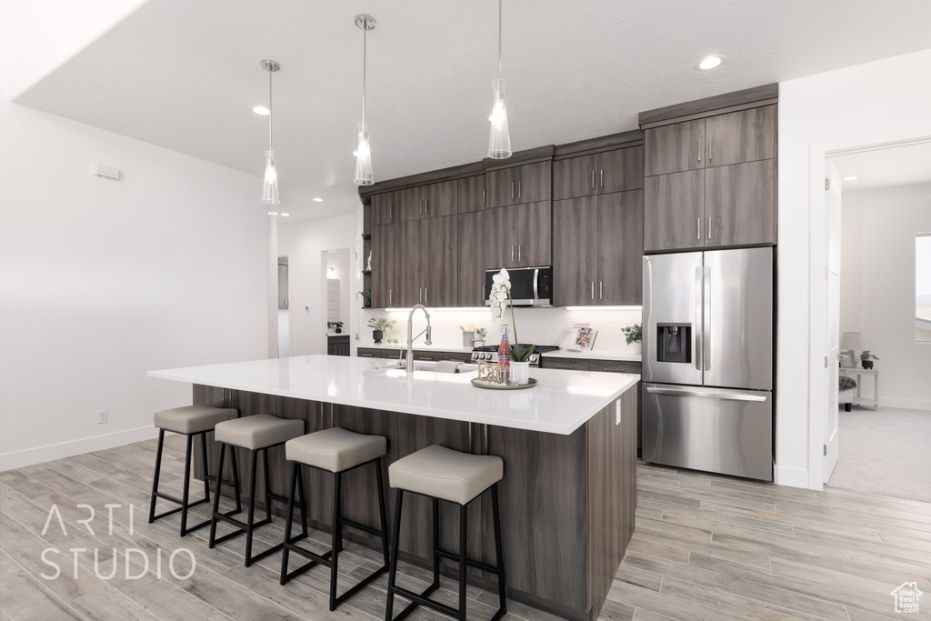 Kitchen with light hardwood / wood-style flooring, appliances with stainless steel finishes, a kitchen island with sink, and sink