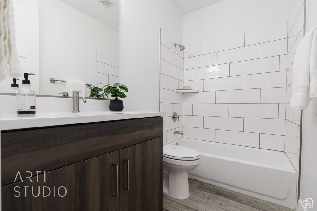 Full bathroom with wood-type flooring, vanity, tiled shower / bath combo, and toilet