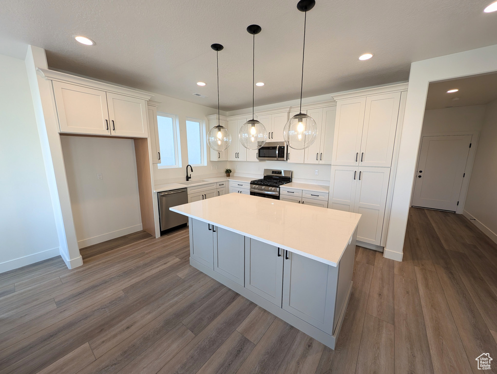 Kitchen with appliances with stainless steel finishes, white cabinetry, a center island, hardwood / wood-style floors, and sink