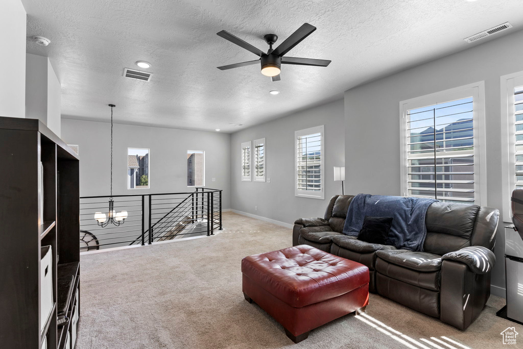 Carpeted living room featuring a textured ceiling and ceiling fan with notable chandelier