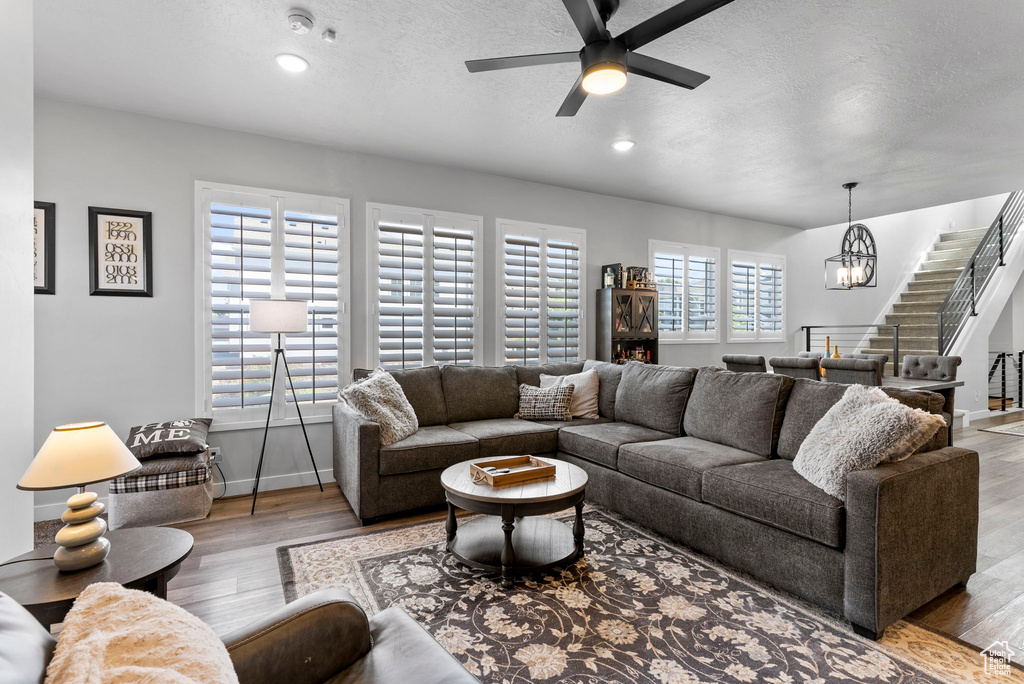 Living room with light hardwood / wood-style flooring, a textured ceiling, and ceiling fan with notable chandelier