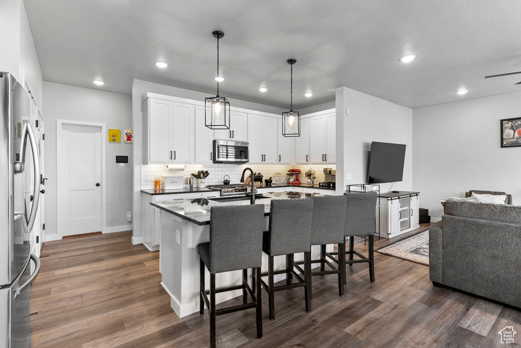 Kitchen with white cabinetry, dark wood-type flooring, backsplash, stainless steel appliances, and a breakfast bar