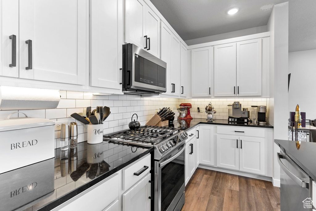 Kitchen with appliances with stainless steel finishes, dark stone countertops, wood-type flooring, and white cabinetry