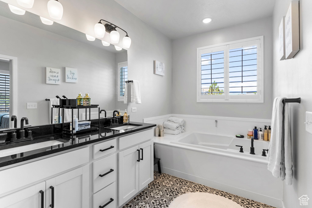 Bathroom with tile patterned flooring, dual bowl vanity, a bathing tub, and a wealth of natural light