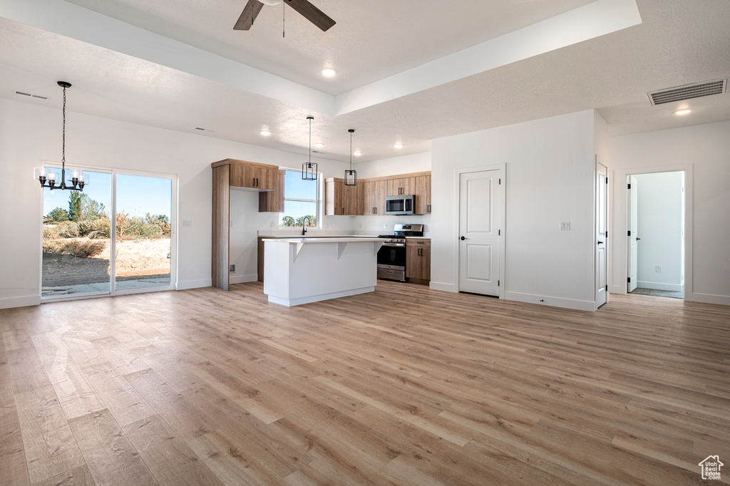 Kitchen featuring a kitchen island, appliances with stainless steel finishes, hanging light fixtures, and light hardwood / wood-style floors