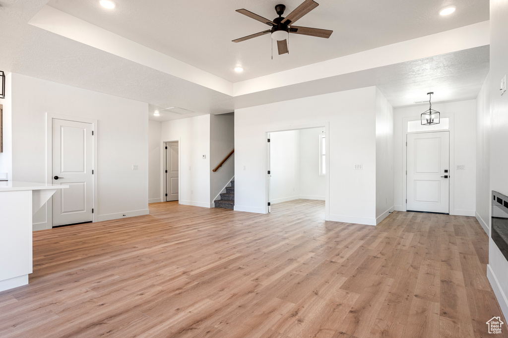 Unfurnished living room with light wood-type flooring and ceiling fan with notable chandelier