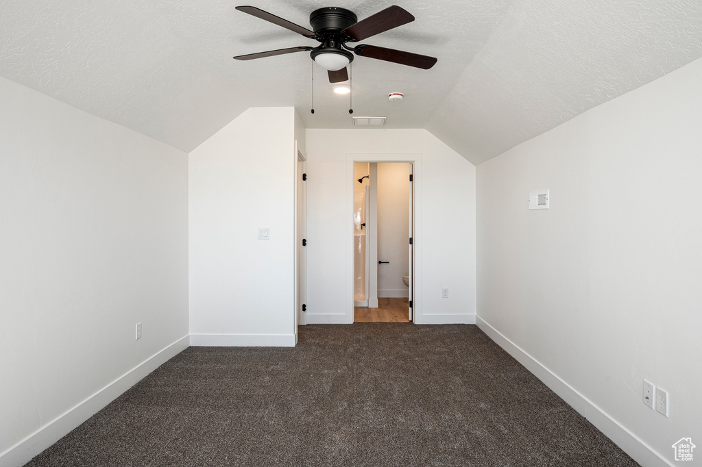 Bonus room with vaulted ceiling, dark colored carpet, and a textured ceiling