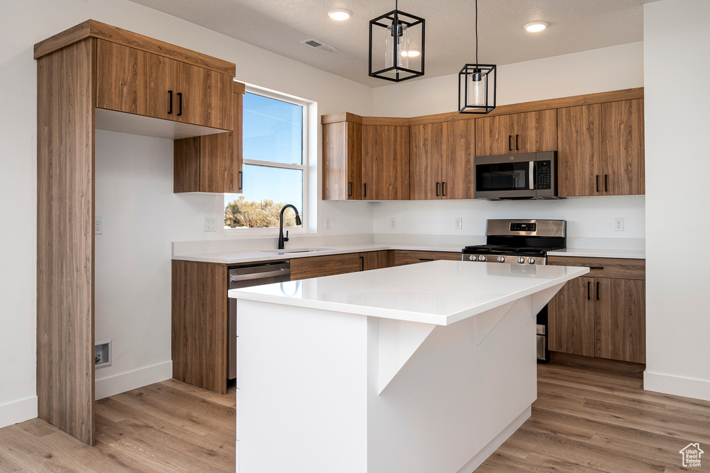 Kitchen with sink, a kitchen island, light hardwood / wood-style floors, stainless steel appliances, and decorative light fixtures