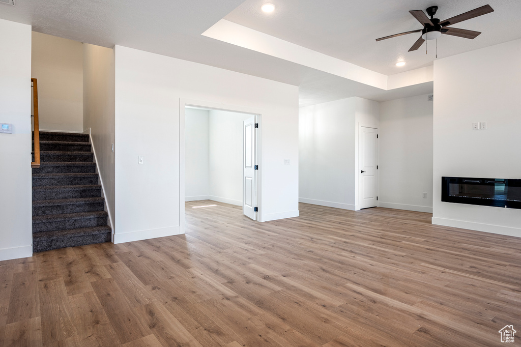 Unfurnished living room featuring light hardwood / wood-style floors, a raised ceiling, and ceiling fan