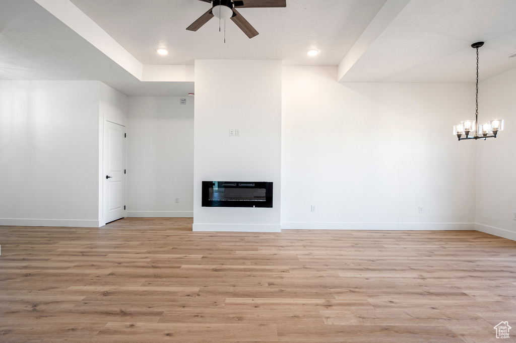 Unfurnished living room featuring light hardwood / wood-style floors, heating unit, and ceiling fan with notable chandelier