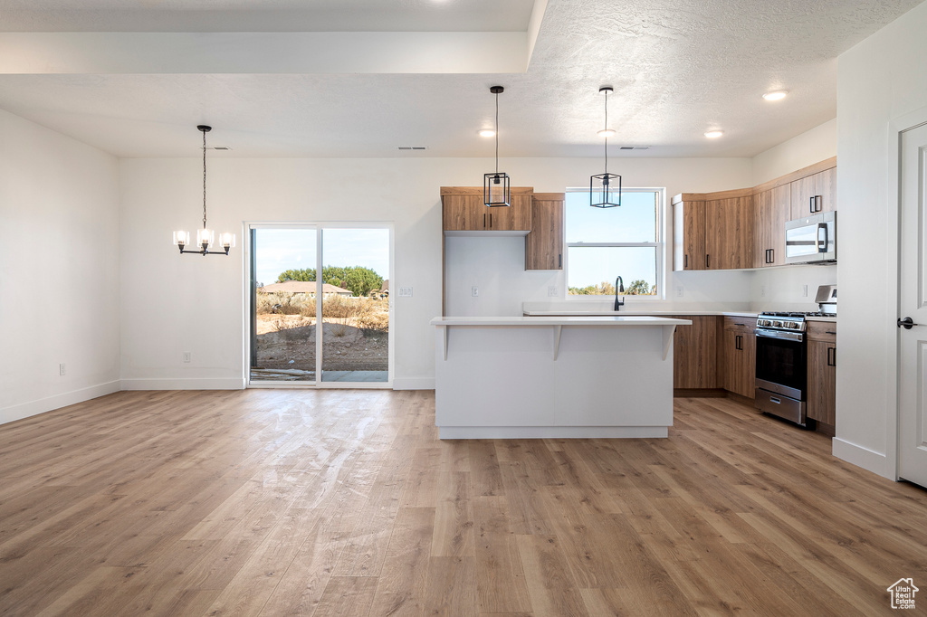 Kitchen with a breakfast bar area, stainless steel appliances, a center island, decorative light fixtures, and light wood-type flooring