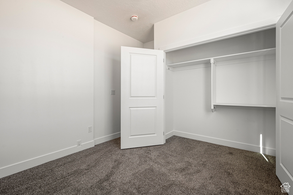 Unfurnished bedroom featuring dark carpet, a textured ceiling, and a closet