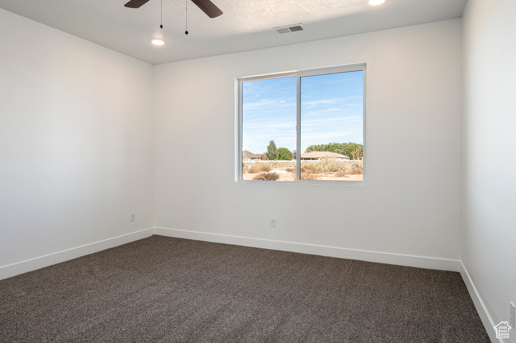 Spare room with a textured ceiling, ceiling fan, and dark colored carpet